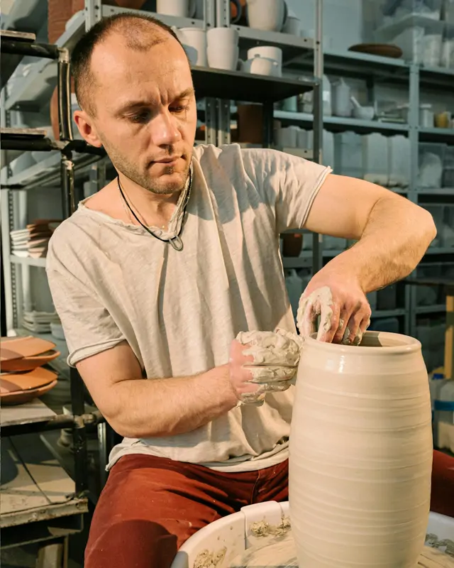 Mann formt einen hohen Tontopf an der Drehscheibe im Töpferkurs